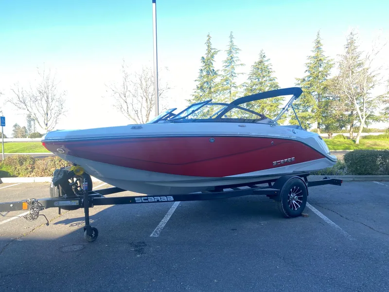 Slide: The Image of 2025 Scarab 195 SE boat on trailer, red and white design, parked outdoors. - 23