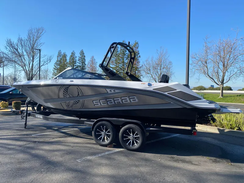 Slide: The Image of 2025 Scarab 235 LX Wake boat on trailer, parked outdoors, side view. - 1