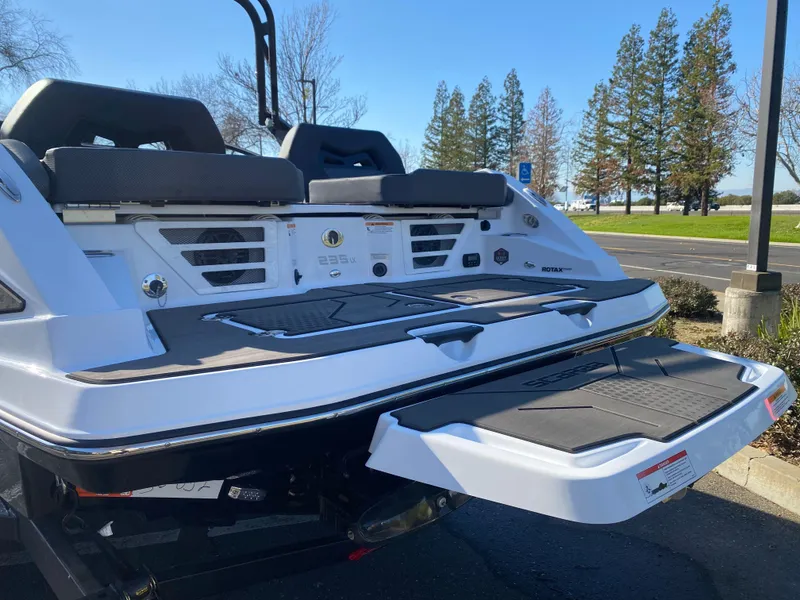 Slide: The Image of 2025 Scarab 235 LX Wake boat rear view with swim platform in a sunny outdoor setting. - 2