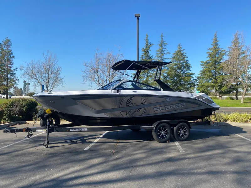 Slide: The Image of 2025 Scarab 235 LX Wake boat on trailer, parked outdoors, clear sky background. - 25