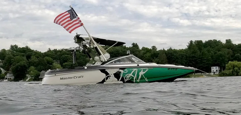 The Image of 2011 MasterCraft XStar boat with American flag on a lake, surrounded by trees. - 1