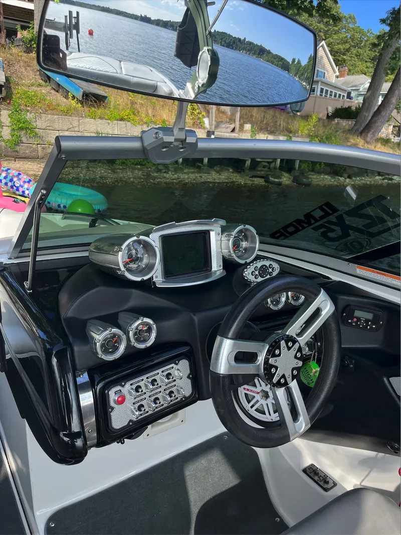 Slide: The Image of 2011 MasterCraft XStar boat dashboard with steering wheel and control panel, near a lake. - 4