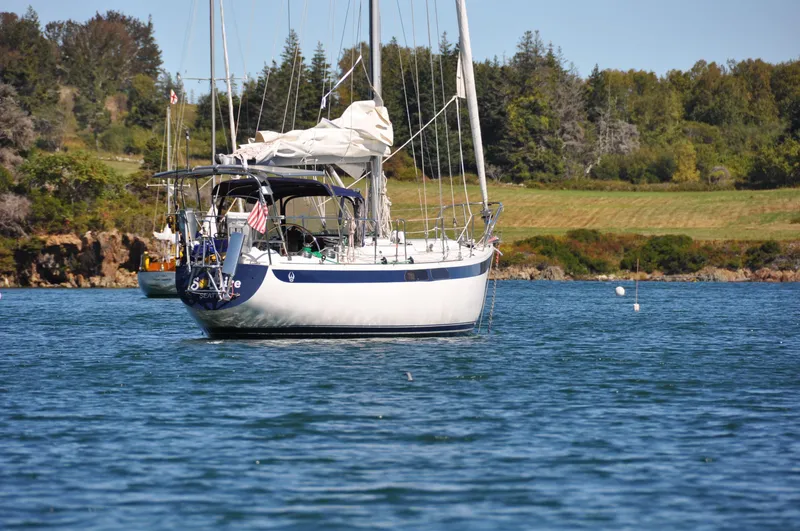 The Image of 1972 Ericson 39 Flushdeck sailboat anchored on a serene lake with lush green shoreline. - 0