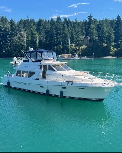 The Image of 2000 McKinna 57 Pilothouse yacht on serene water with forested background. - 0