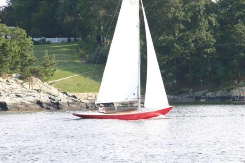 Slide: The Image of Red Rustler 24 sailboat from 2025 sailing near a rocky shoreline with lush greenery. - 4