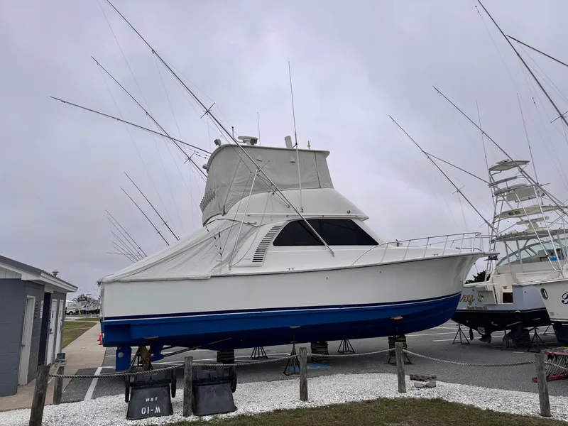 Slide: The Image of 2011 Henriques 42 Sportfisherman boat on land, white and blue hull, fishing rods visible. - 14