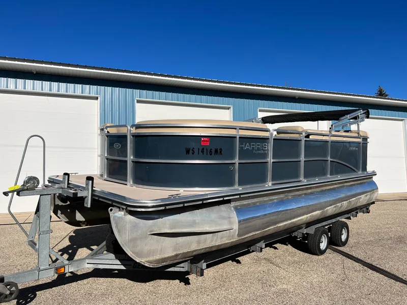 Slide: The Image of 2013 Harris FloteBote Cruiser pontoon boat on trailer, parked outside a blue building. - 6