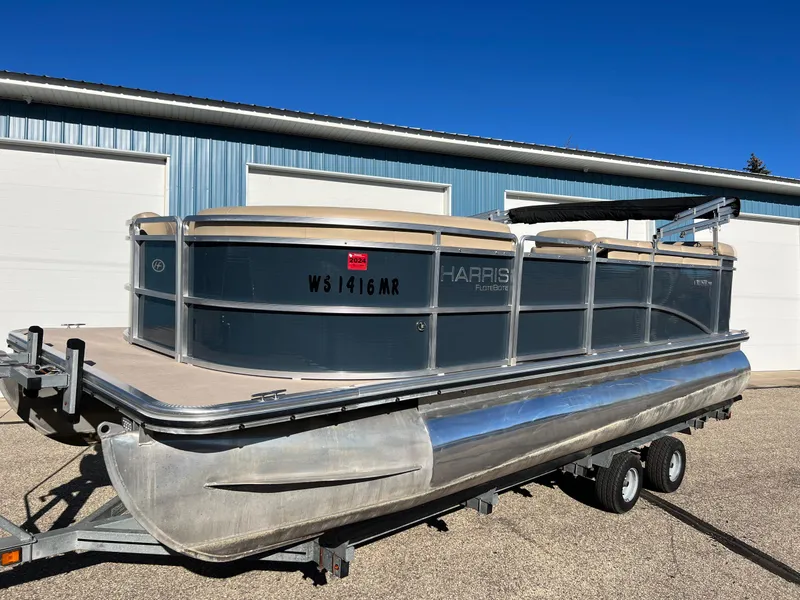Slide: The Image of 2013 Harris FloteBote Cruiser pontoon boat on trailer, parked outside a blue building. - 7