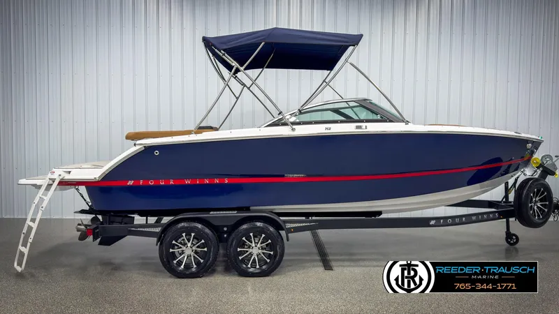 Slide: The Image of 2025 Four Winns H2 boat on trailer, blue hull, red stripe, under canopy, in showroom. - 5