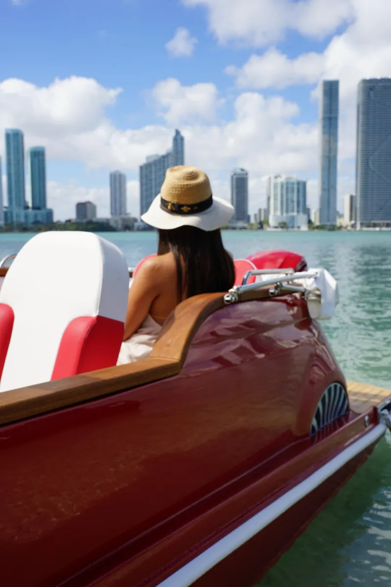 Slide: The Image of Woman in a hat on a classic Fiat 500 boat, city skyline in background. - 15