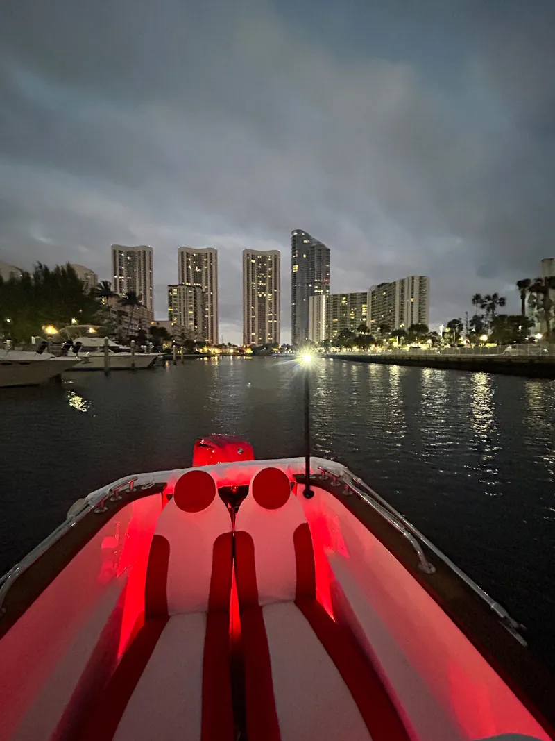 Slide: The Image of Boat with red interior lights on water, city skyline in background at dusk. - 19