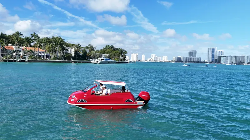 Slide: The Image of Red Car Off-shore Fiat 500 Classic boat on blue water, city skyline in background, 2025 model. - 3