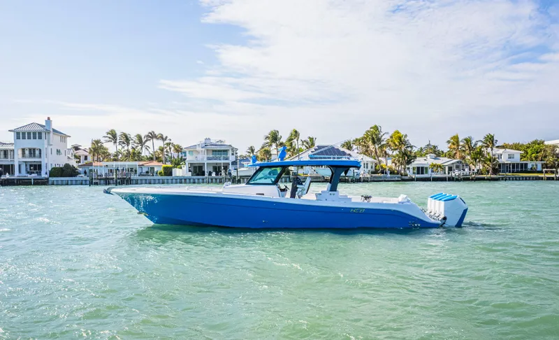 Slide: The Image of 2025 HCB 48 Campeon boat cruising on a sunny day near waterfront homes. - 1
