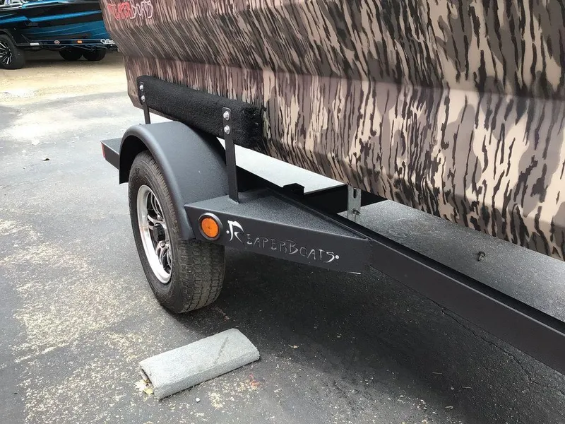 Slide: The Image of Trailer of 2025 Reaper Boats 656 with camouflage design parked on pavement. - 18