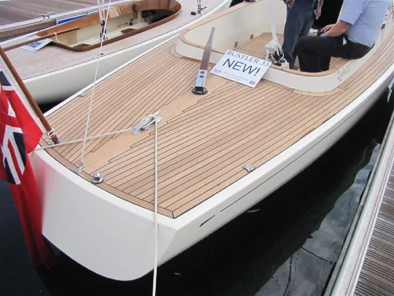 Slide: The Image of 2025 Rustler 33 sailboat with teak deck, docked, featuring a "NEW" sign and a red flag. - 12