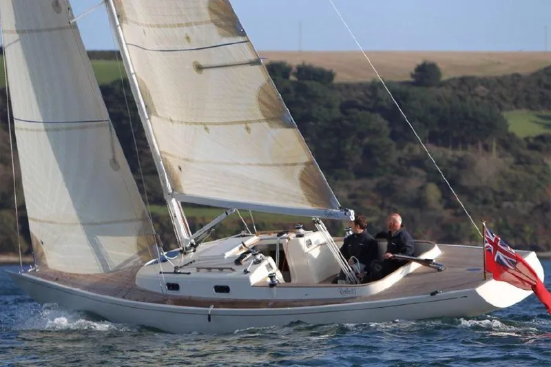 Slide: The Image of 2025 Rustler 33 sailboat navigating coastal waters with two people onboard. - 5