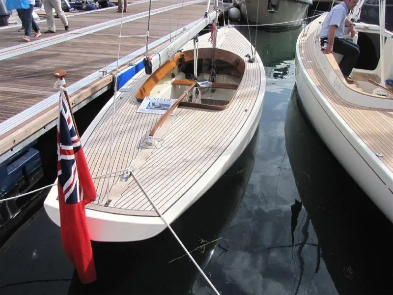 Slide: The Image of 2025 Rustler 33 sailboat docked, featuring sleek wooden deck and red ensign flag. - 9