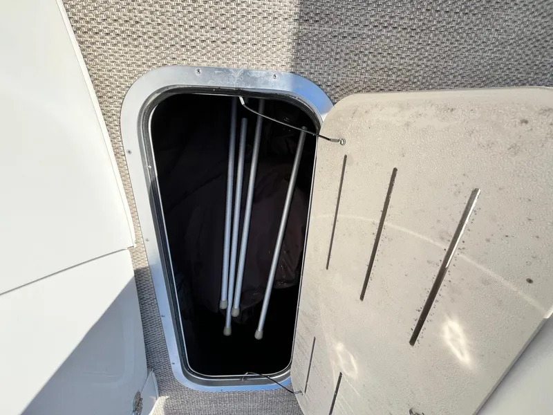 Slide: The Image of Open storage compartment on 2023 Bennington 23Q boat, showing interior space and poles. - 26