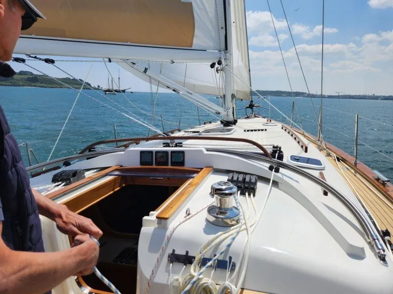 Slide: The Image of Sailing on a 2025 Rustler 37 yacht, clear skies, open sea, and a person adjusting ropes. - 12