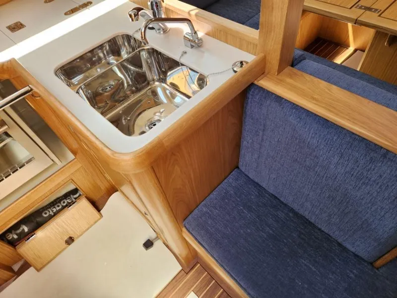 Slide: The Image of 2025 Rustler 37 yacht interior with wooden finish, blue seating, and stainless steel sink. - 31