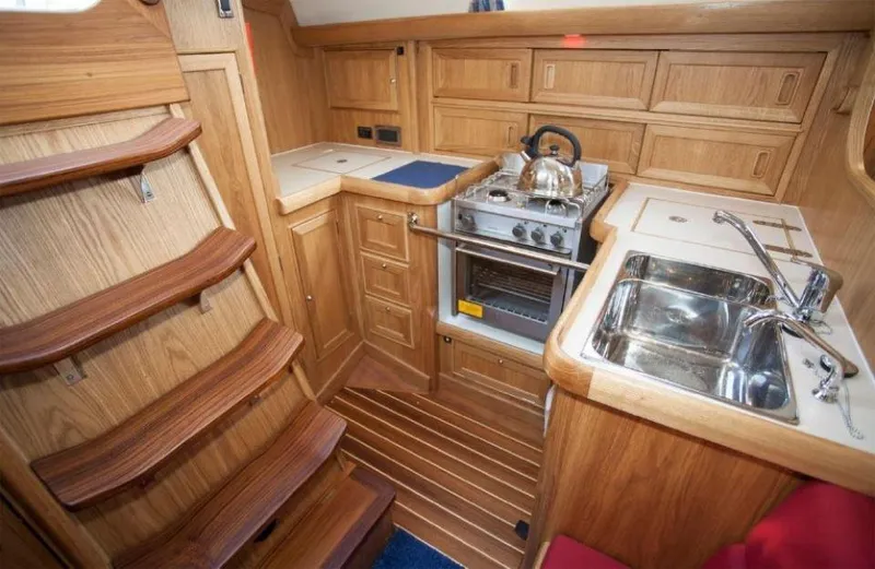 Slide: The Image of 2025 Rustler 37 yacht interior with wooden cabinetry, compact kitchen, and stainless steel sink. - 32