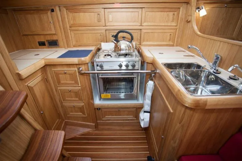 Slide: The Image of Rustler 37 yacht kitchen interior, featuring wooden cabinetry, stove, and dual sink, 2025 model. - 33