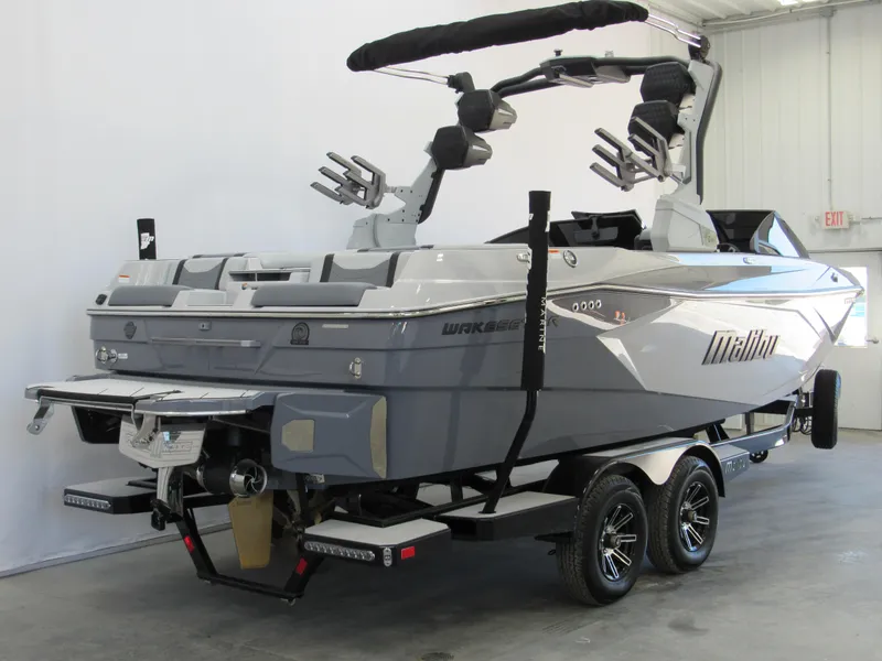 Slide: The Image of 2025 Malibu 23 LSV boat in showroom, sleek gray design, dual-axle trailer. - 2