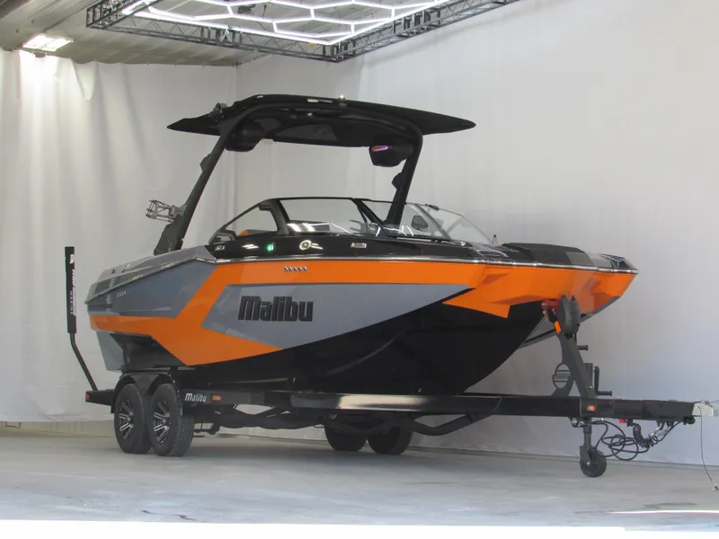 Slide: The Image of 2025 Malibu Wakesetter 22 MXZ boat in showroom, vibrant orange and gray design. - 2