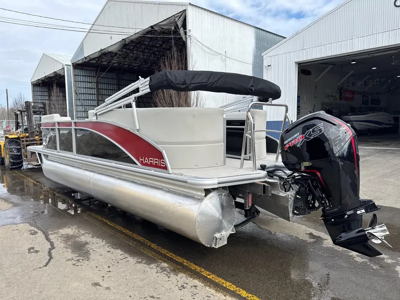 Slide: The Image of 2025 Harris Breeze 230 pontoon boat with outboard motor, parked near industrial buildings. - 2