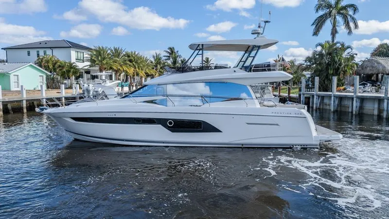 The Image of 2021 Prestige 520 Flybridge yacht cruising near waterfront homes and palm trees. - 0