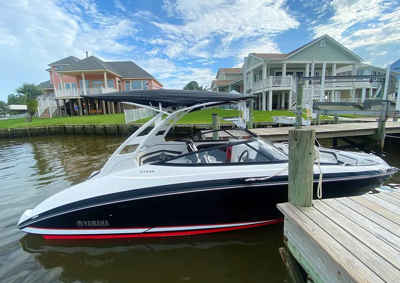 Slide: The Image of 2020 Yamaha Boats 242 Limited SE docked by waterfront homes under a blue sky. - 21