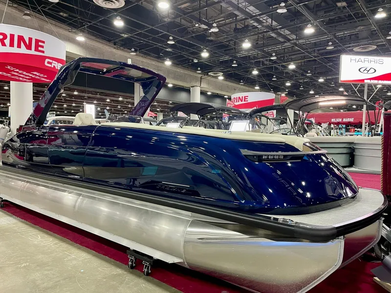 Slide: The Image of 2025 Harris Crowne SL 250 pontoon boat displayed at an indoor boat show. - 0