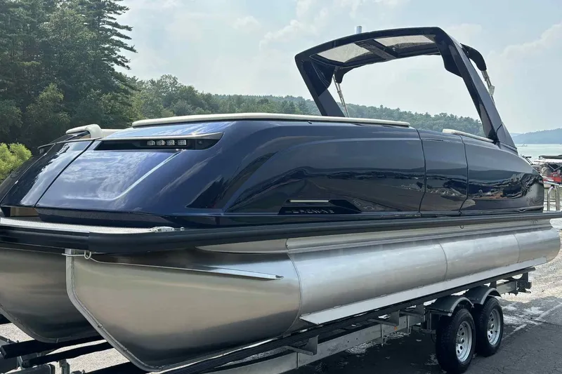 Slide: The Image of 2025 Harris Crowne SL 250 pontoon boat on trailer, sleek design, forest backdrop. - 11