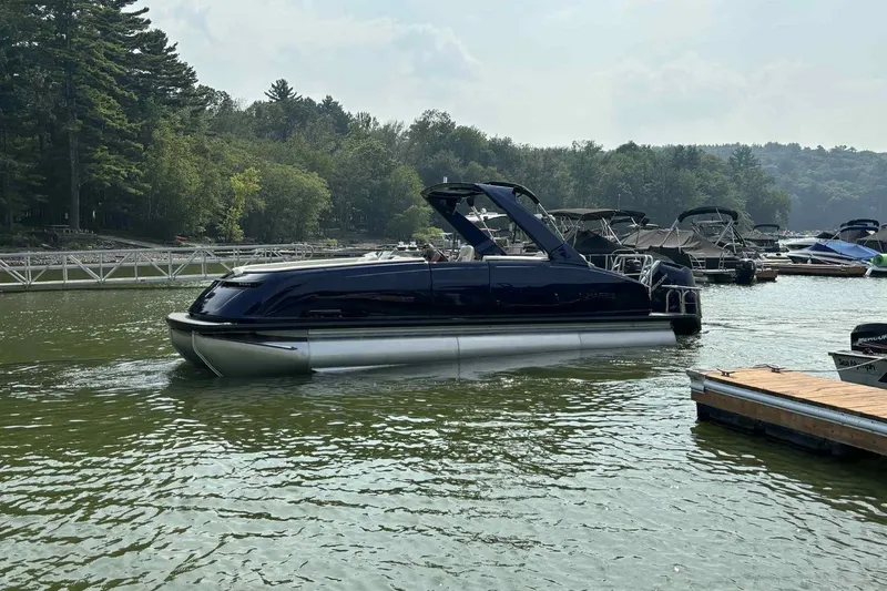 Slide: The Image of 2025 Harris Crowne SL 250 pontoon boat on a serene lake near a dock. - 12
