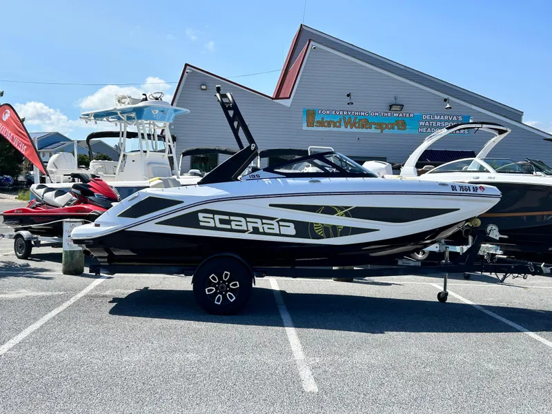 The Image of 2024 Scarab 195 ID boat in a parking lot, sunny day, dealership background. - 0