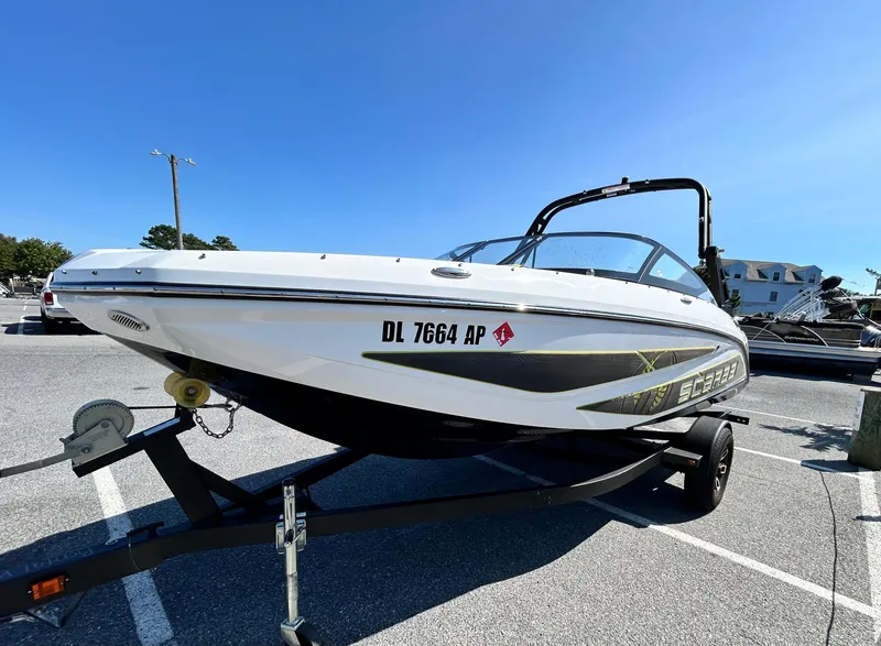Slide: The Image of 2024 Scarab 195 ID boat on trailer in parking lot under clear blue sky. - 2