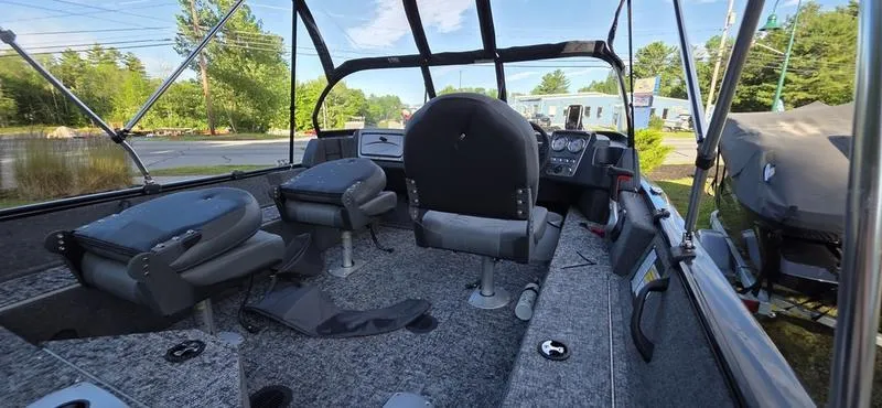 Slide: The Image of 2025 Tracker PG V16 WT boat interior with seating and dashboard, surrounded by trees and buildings. - 7