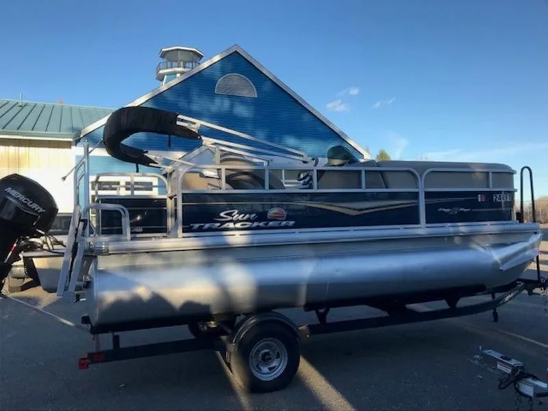 Slide: The Image of 2022 Sun Tracker PB 18 DLX pontoon boat on trailer, parked near blue building. - 6