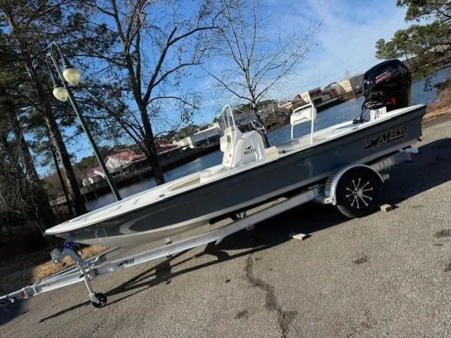 Slide: The Image of 2025 Mako 18 LTS boat on trailer by a lakeside, under clear blue sky. - 0
