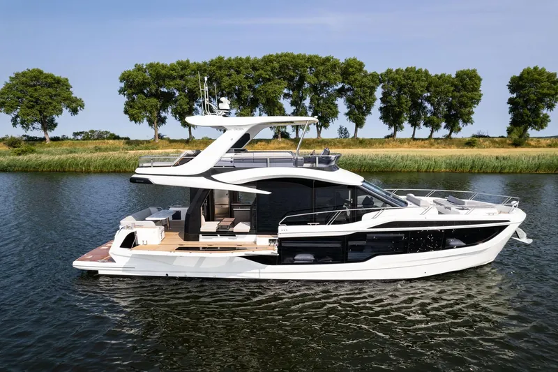 Slide: The Image of 2025 Galeon 560 Fly yacht cruising on a serene river with lush green trees. - 2