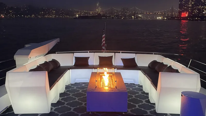 Slide: The Image of Luxurious 1987 Guy Couach 97 yacht deck with cozy seating and fire pit, city skyline backdrop. - 16