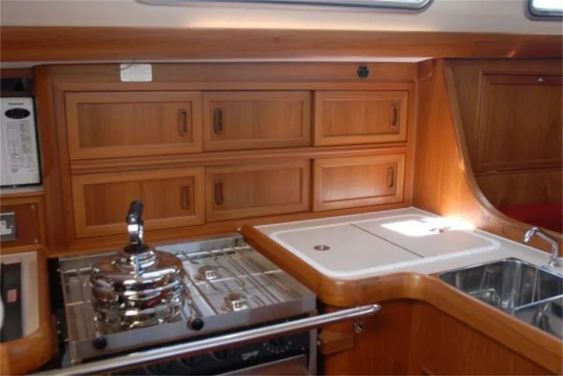 Slide: The Image of 2025 Rustler 42 yacht interior kitchen with wooden cabinets, stove, and sink. - 20