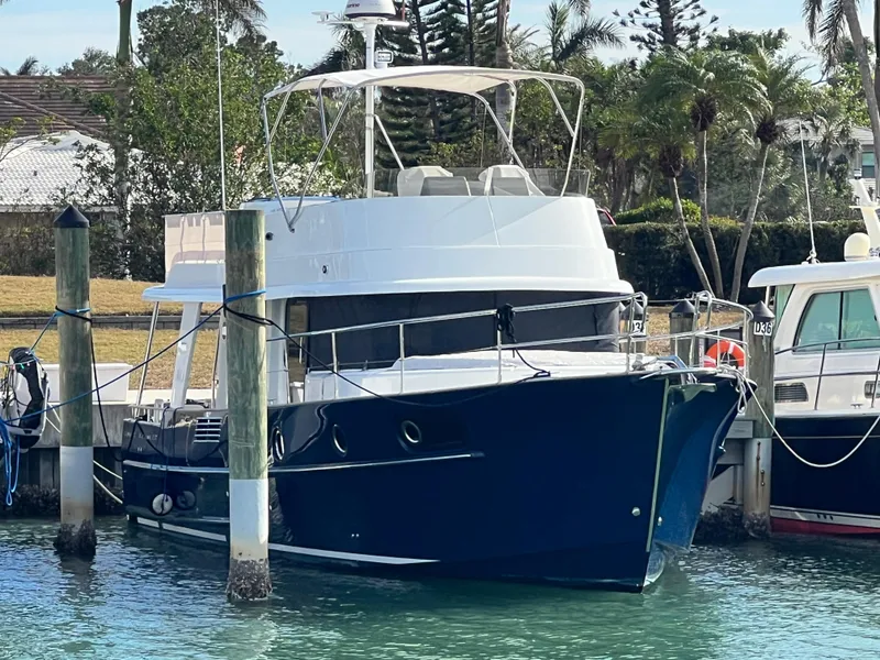 Slide: The Image of 2019 Beneteau Swift Trawler 44 docked in a marina, surrounded by lush greenery. - 1
