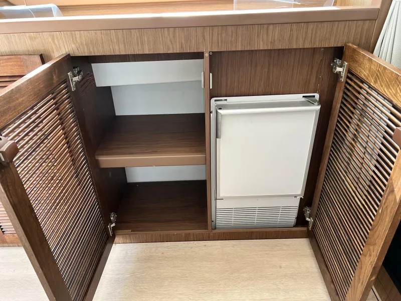 Slide: The Image of Wooden cabinet with open doors and a small built-in refrigerator on a 2019 Beneteau Swift Trawler 44. - 13