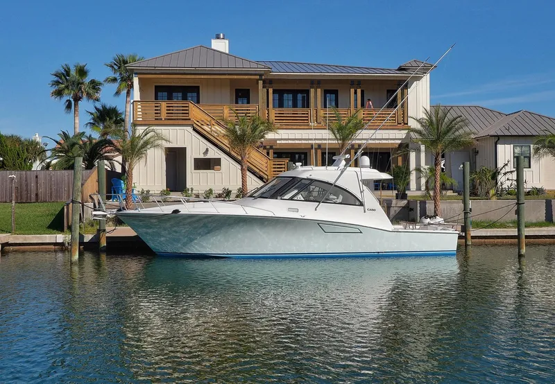 Slide: The Image of 2013 Cabo HTX yacht docked by a waterfront house with palm trees. - 1