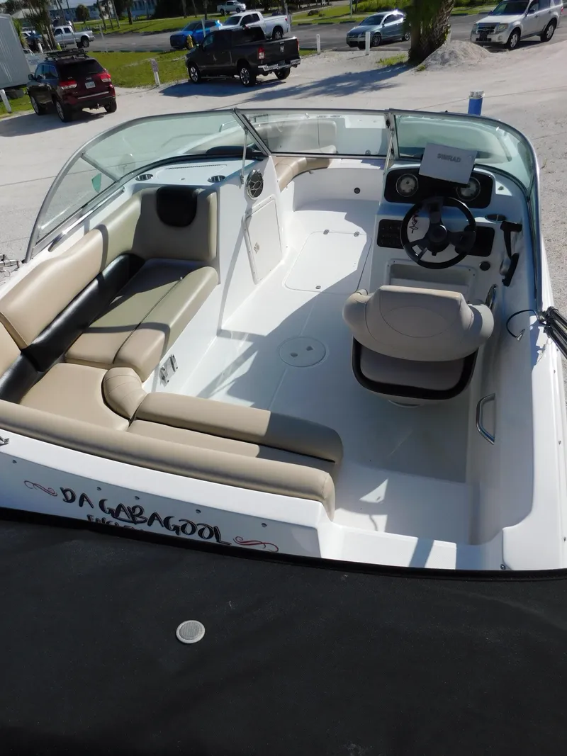 Slide: The Image of 2015 Hurricane SunDeck 187 OB boat with beige seating and steering wheel, parked on a trailer. - 12