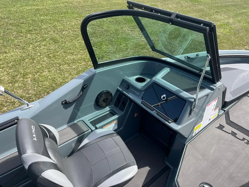 Slide: The Image of 2025 Lund 185 Impact GL boat interior with steering console and seating on grassy background. - 29