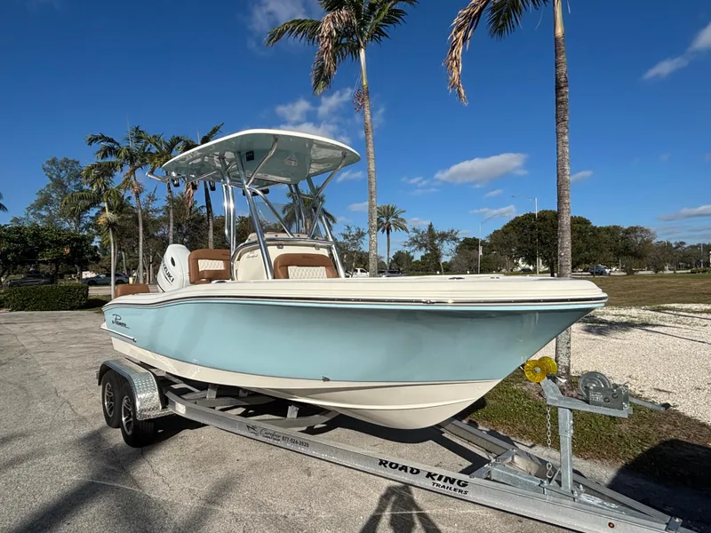 Slide: The Image of 2025 Pioneer 202 Sportfish boat on trailer, parked outdoors under palm trees. - 2