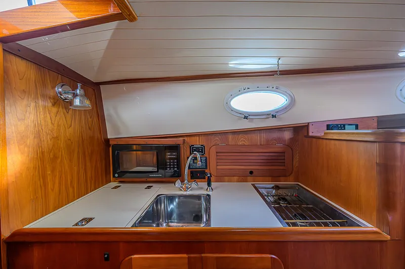 Slide: The Image of 2000 Hinckley Picnic Boat Classic interior with wooden cabinetry, sink, stove, and microwave. - 15
