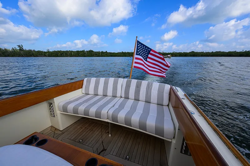 Slide: The Image of Hinckley Picnic Boat Classic 2000 with American flag, cruising on a serene lake under blue skies. - 6